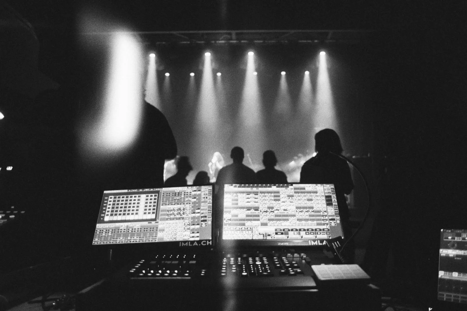A lighting desk overlooking a stage, with beams of light above the audience.